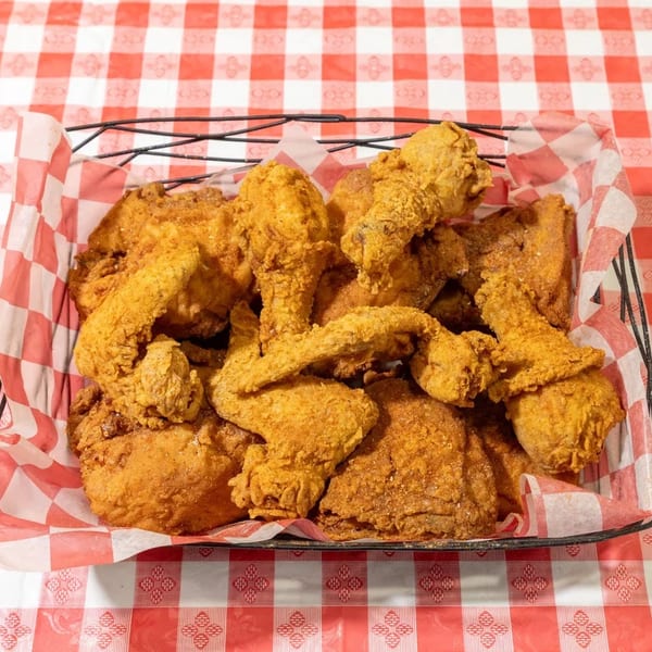 A wire basket filled with crispy fried chicken pieces on a red and white checkered tablecloth.