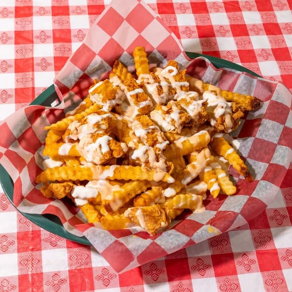 Crinkle-cut fries topped with crispy chicken pieces and drizzled with white and orange sauces.