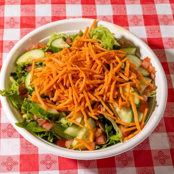 Fresh garden salad with lettuce, cucumbers, tomatoes, and shredded carrots on a red and white checkered tablecloth.