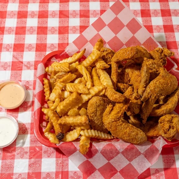 A red basket of crispy fried chicken wings and crinkle-cut fries with two dipping sauces.