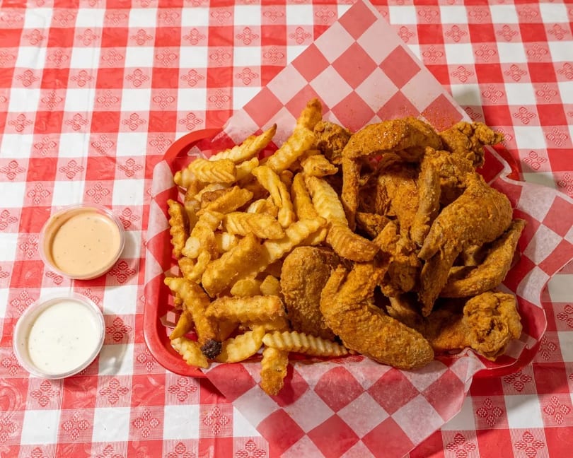 A red basket of crispy fried chicken wings and crinkle-cut fries with two dipping sauces.