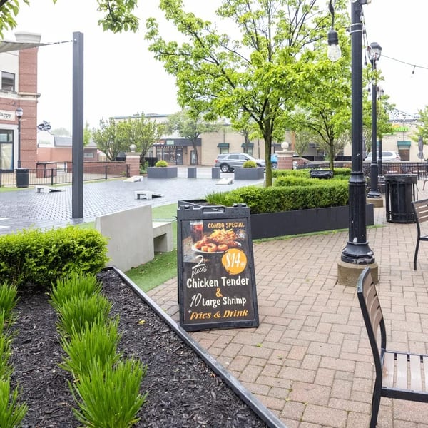 A restaurant combo special sign for chicken tenders and shrimp on a brick patio with outdoor seating.