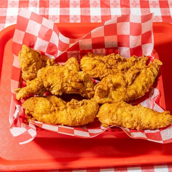 Golden fried chicken tenders in a red basket with checkered paper, on a red and white tablecloth.