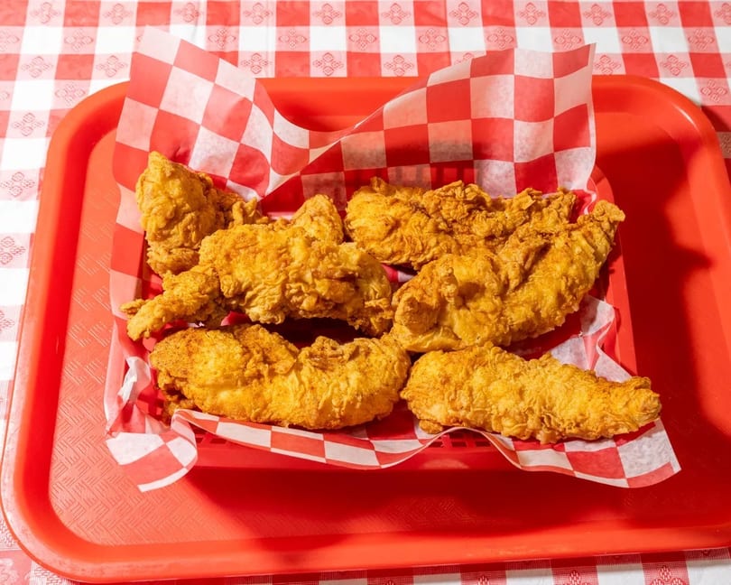 Golden fried chicken tenders in a red basket with checkered paper, on a red and white tablecloth.