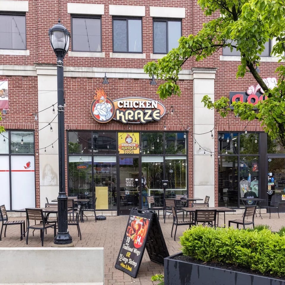 Chicken Kraze restaurant exterior with outdoor seating, brick facade, and a promotional sign for wings and shrimp.