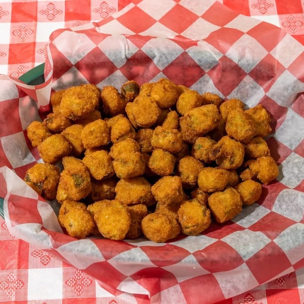 A basket of golden-brown fried okra sits on a red and white checkered tablecloth.