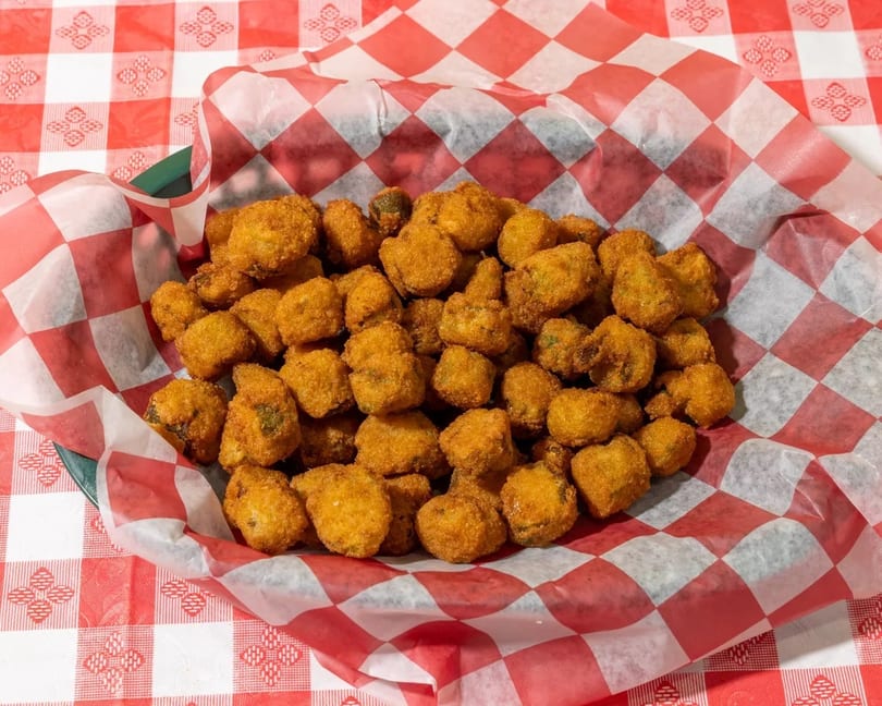 A basket of golden-brown fried okra sits on a red and white checkered tablecloth.