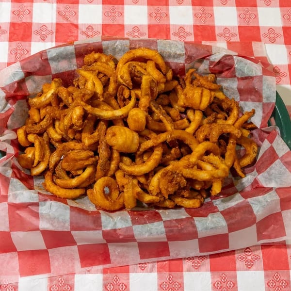 A basket of golden curly fries with seasoning, served on a red and white checkered tablecloth.
