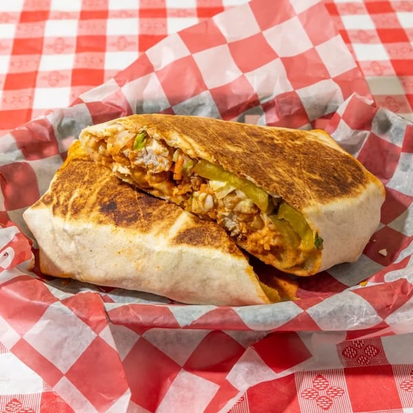 A grilled burrito, cut in half, revealing its filling, served in red and white checkered paper.