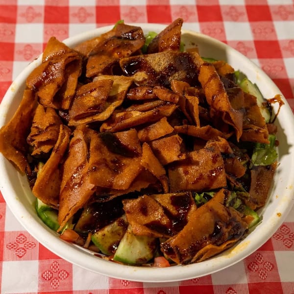 Fattoush salad with crispy pita bread, fresh vegetables, and a dark dressing on a red and white checkered tablecloth.