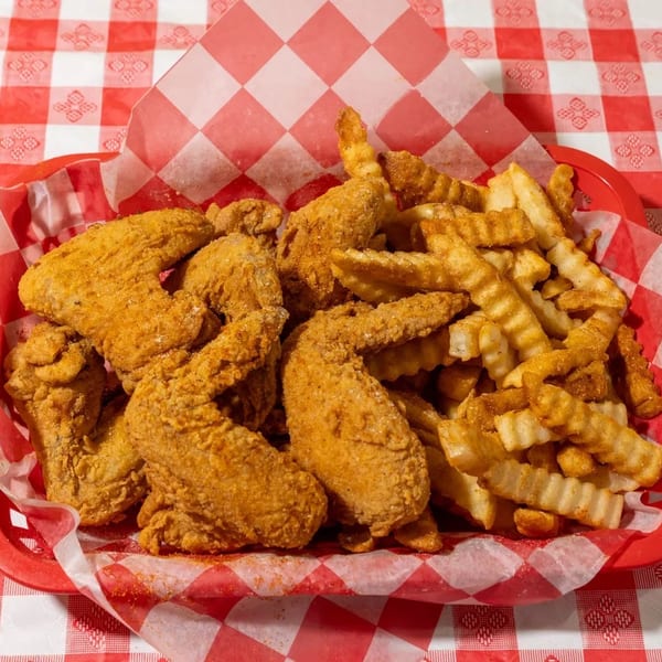 Crispy fried chicken wings and crinkle-cut fries in a red basket with checkered paper lining.